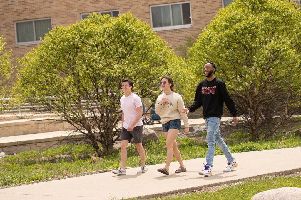 Three students walking on the sidewalk by residence halls.