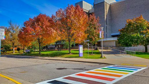 Albertson Hall fall colors on trees behind rainbow pridewalk